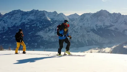 Zwei Skifahrer vor einer verschneiten Bergkulisse