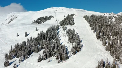 Verschneite Skipisten am Berghang mit Nadelwald und Skilift