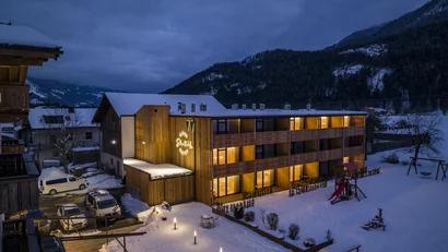 Beleuchtetes Holz-Hotel in einer verschneiten Berglandschaft bei Dämmerung