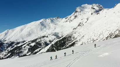 Skifahrer steigen vor schneebedeckten Bergen einen Hang hinauf