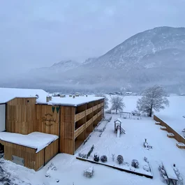 Holzgebäude und verschneiter Garten vor einem nebligen Berg