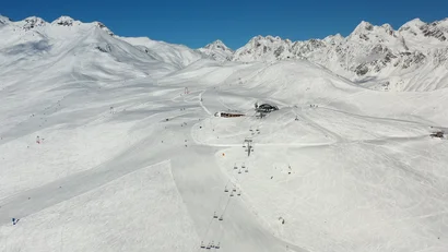 Verschneite Skipisten mit Skiliften vor einer Bergkulisse unter blauem Himmel